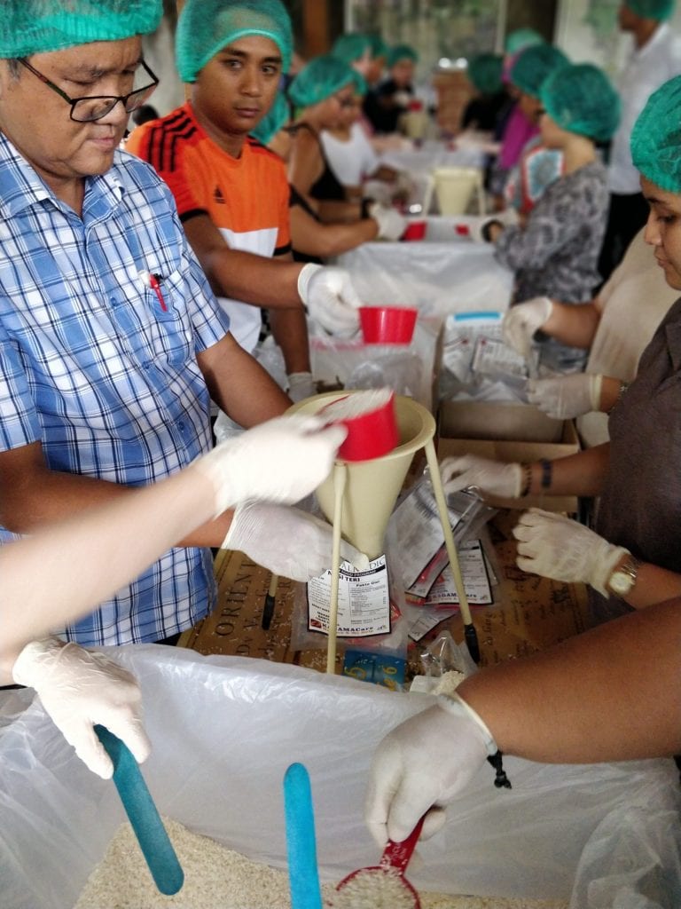 Volunteers scooping rice into a funnel