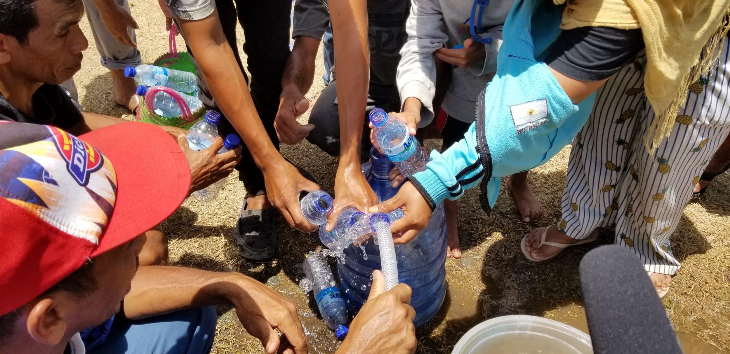 People holding out bottles to get water from a hose.