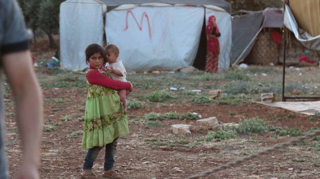 Standing in front of a tent a young girl holds a baby