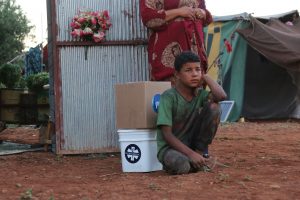 A Syrian IDP sits with a GlobalMedic Emergency Food Kit and Family Emergency Kit