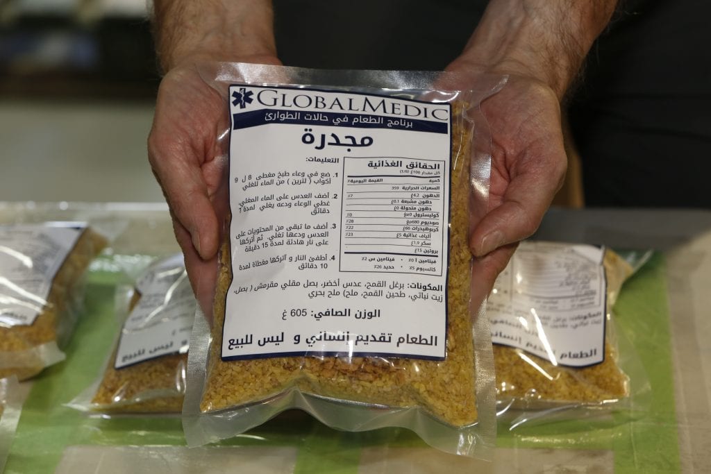Hands holding an Emergency Food Kit containing the meal Mujaddara