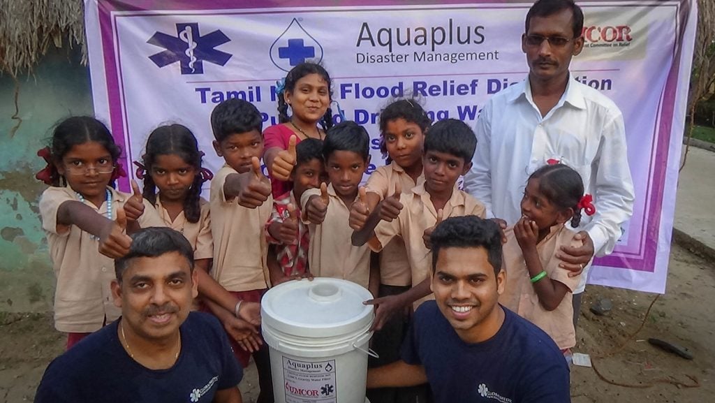 Two Rapid Response Team members with a group of children holding a household water purification unit