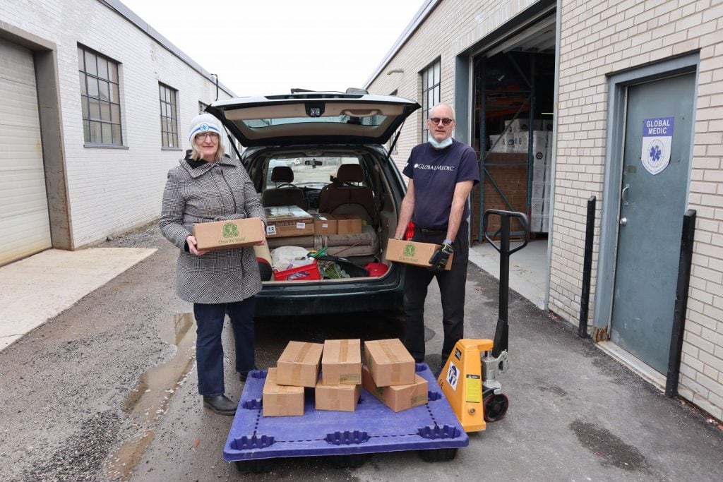 A man and a woman standing in front of a car holding boxes of soap