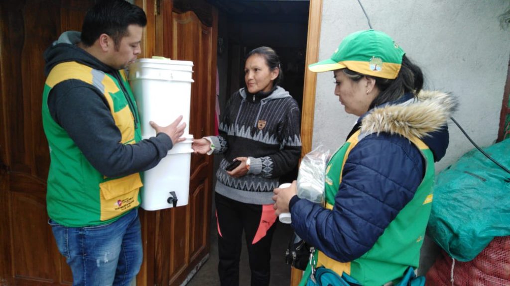 A man hands a water purification unit to a woman while another woman looks on